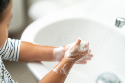Small child washing her hands with soap in the sink.
