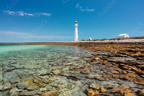 rocky shore with lighthouse and outbuildings under blue sky photo