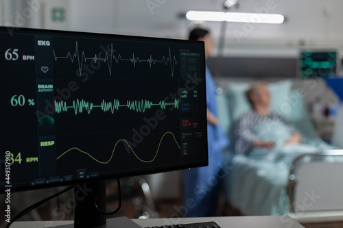 Foto Monitor in hospital ward showing bmp from patient, laying in bed with oxymeter attached on finger, discussing with doctor and nurse about recovery treatment