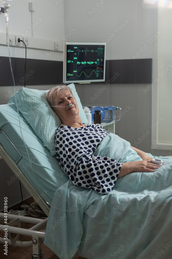 Portrait of senior woman smiling looking at camera laying in hospital bed betting treatment through iv drip bag. Breathing with help from oxygen mask during illness recovery. Portrait of senior woman smiling looking at camera laying in hospital bed betting treatment through iv drip bag. Breathing with help from oxygen mask during illness recovery.