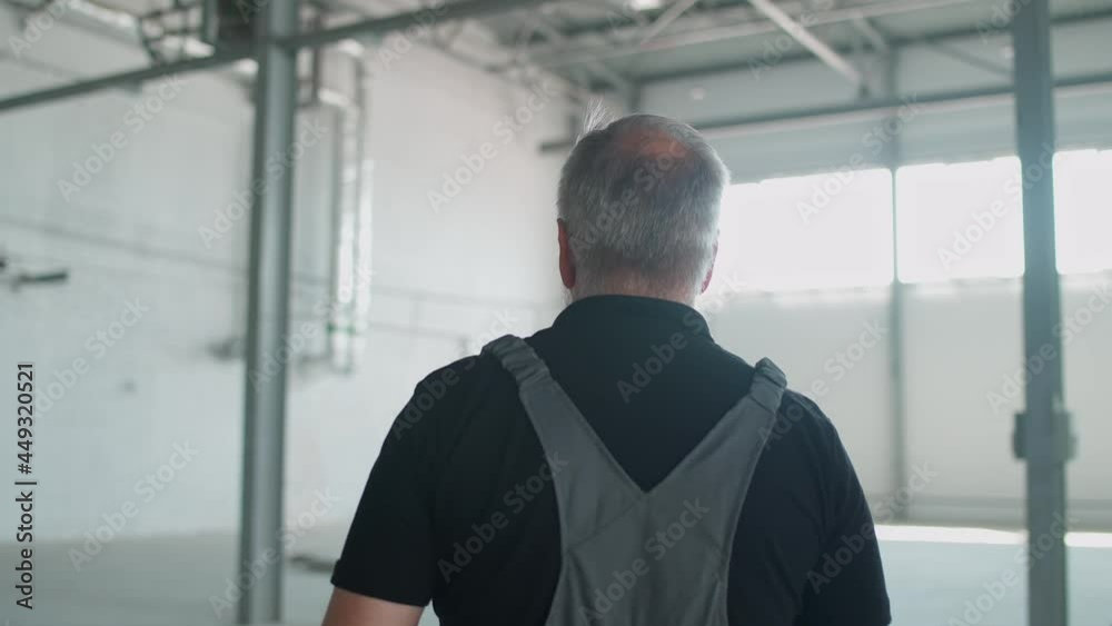 Back view of gray-haired man worker walks through the warehouse, a engineer walks through the territory of an empty logistics warehouse.