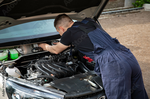 a man repairs a car. a man in blue special clothes to repair the car. engine parts machine repair maintenance breakage problem hands people man master