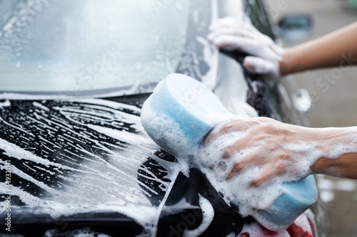 He was washing a black car with a blue sponge.