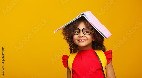 Tableau sur toile funny smiling Black child school girl with glasses hold books on her head