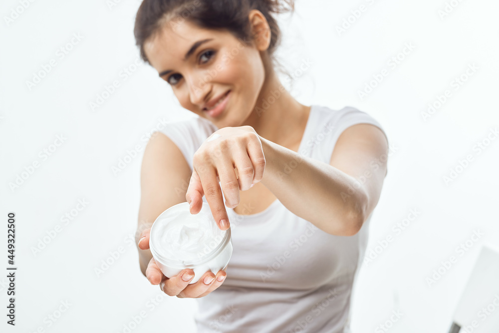 cheerful brunette in a white t-shirt with a jar of cream in her hands skin care light background cheerful brunette in a white t-shirt with a jar of cream in her hands skin care light background