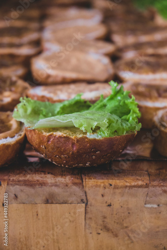 Burger bread placed on a cutting board. Cutting board with slices of bread with sesame seeds for making burgers. Sandwiches with sesame for ground meat or grilled meat. Sandwiches with salad on top.