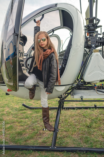 Preteen girl in mirrored sunglasses standing on footboard of open helicopter photo