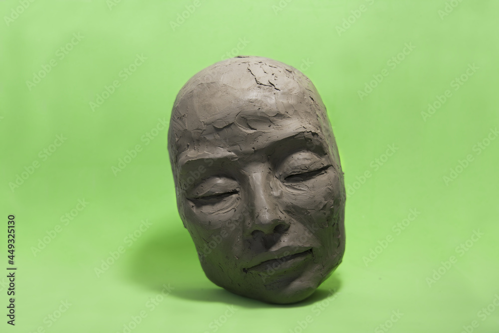 Female face in clay on green background. Sculpture with Caucasian features, closed eyes, calm expression: in process of creation. Female face in clay on green background. Sculpture with Caucasian features, closed eyes, calm expression: in process of creation.