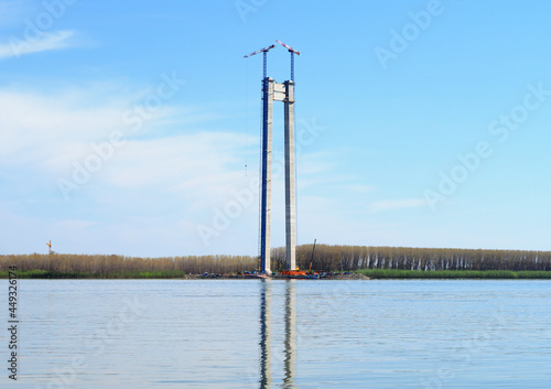 Concrete pillars for suspension bridge under construction with crane under the river