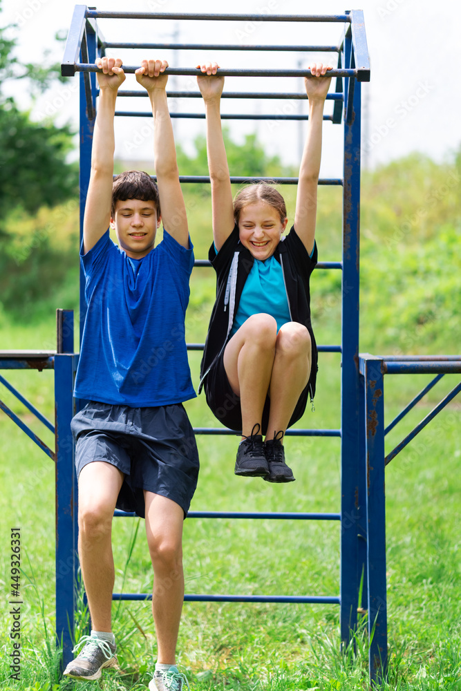 Fototapeta premium teenage boy and girl exercising outdoors, sports ground in the yard, they posing at the horizontal bar, healthy lifestyle