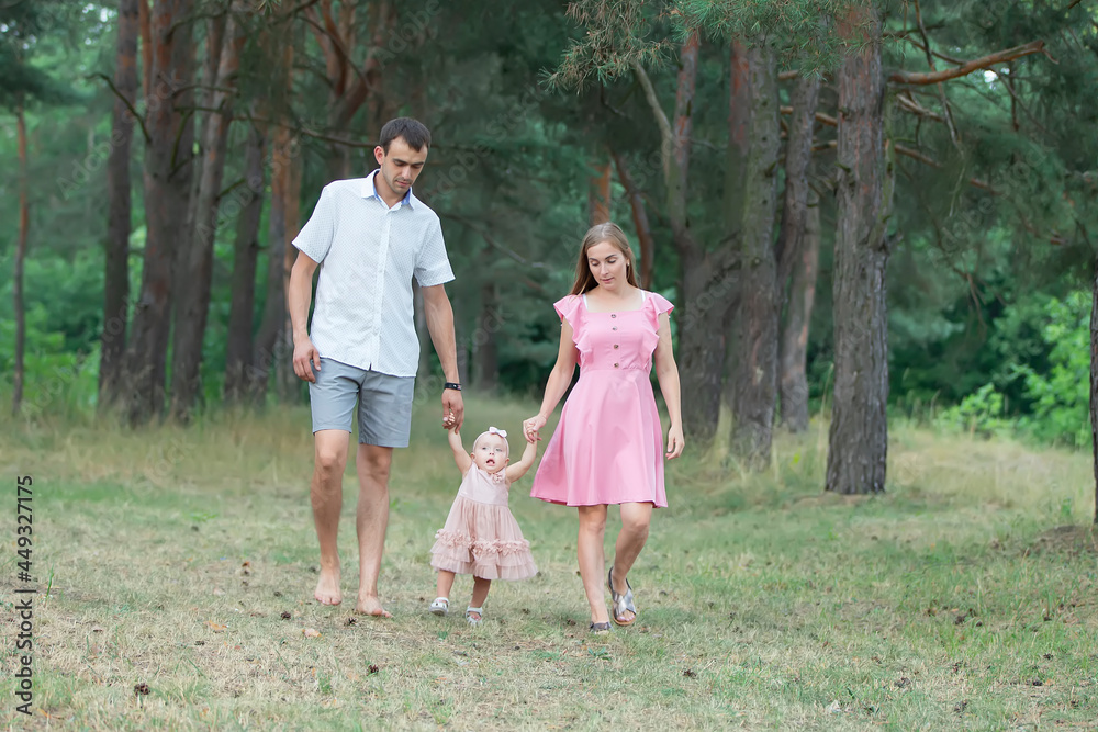 Husband, wife and their little daughter for a walk in the park. Happy dad and mom are walking through the woods with their one-year-old daughter. Husband, wife and their little daughter for a walk in the park. Happy dad and mom are walking through the woods with their one-year-old daughter.