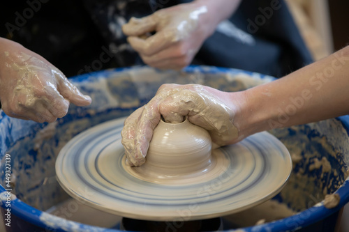 The potter teaches the craft to the child. Close-up of a potter's hands and a child's hand with a product on a potter's wheel. Working with clay. Clay master class.