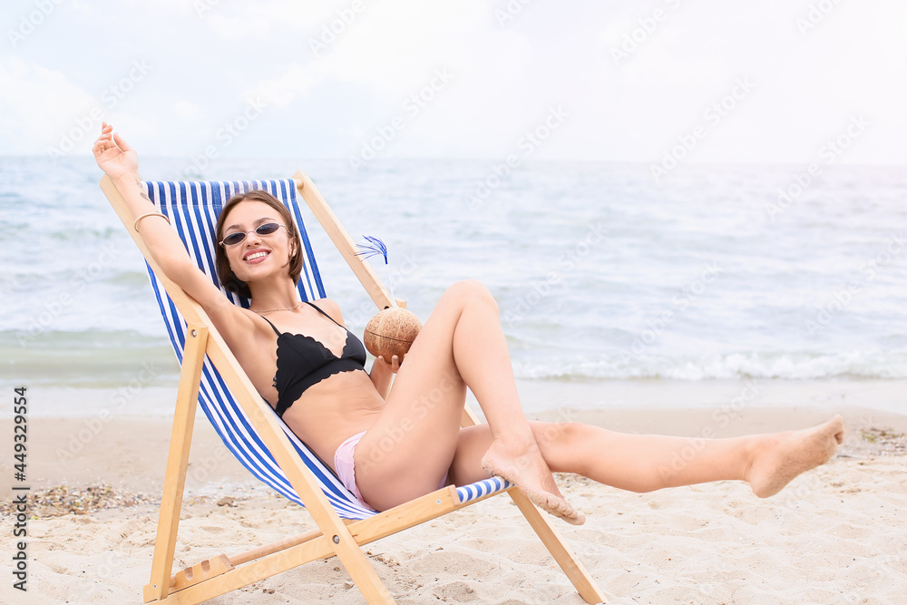 Beautiful young woman drinking coconut milk on sea beach