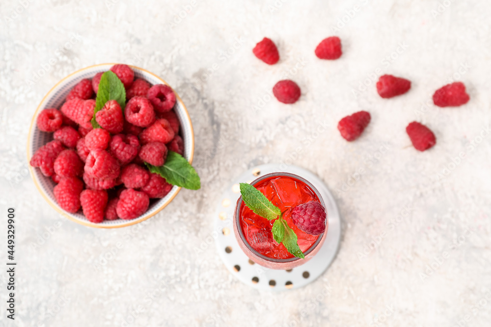 Glass of delicious lemonade and bowl with raspberry on light background Glass of delicious lemonade and bowl with raspberry on light background