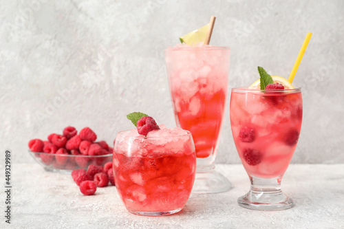 Glasses of cold lemonade with raspberry on light background