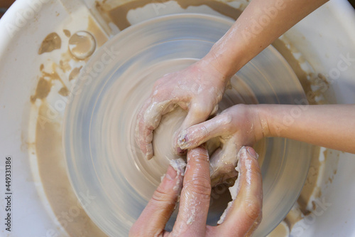 Close-up of a potter's hands and a child's hand with an item on a potter's wheel. Working with clay. Clay workshop. Craft training.