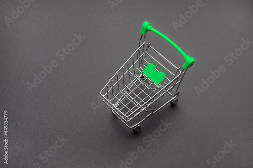 Empty miniature supermarket trolley on a black background. Concept of buying and selling goods. Online sales on the Internet. Selective focus, copy space.