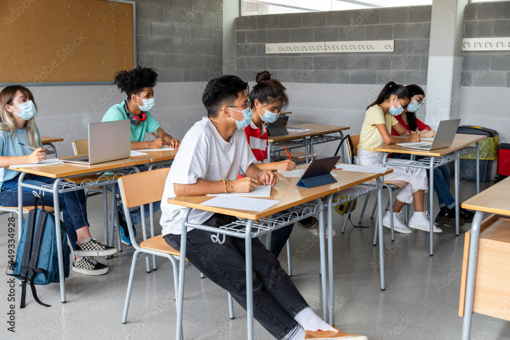 Group of multiracial teenager high school students in class wearing protective face masks.