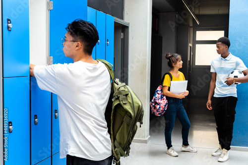 Teen asian high school student putting books away in lockers. Teenagers talking in school corridor. photo