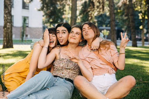 Group of four women friends sitting in a park, hugging and laughing. Concept of female friendship.