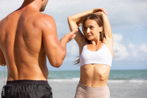 young woman stretching and exercising outdoors from trainer suggesting on the beach