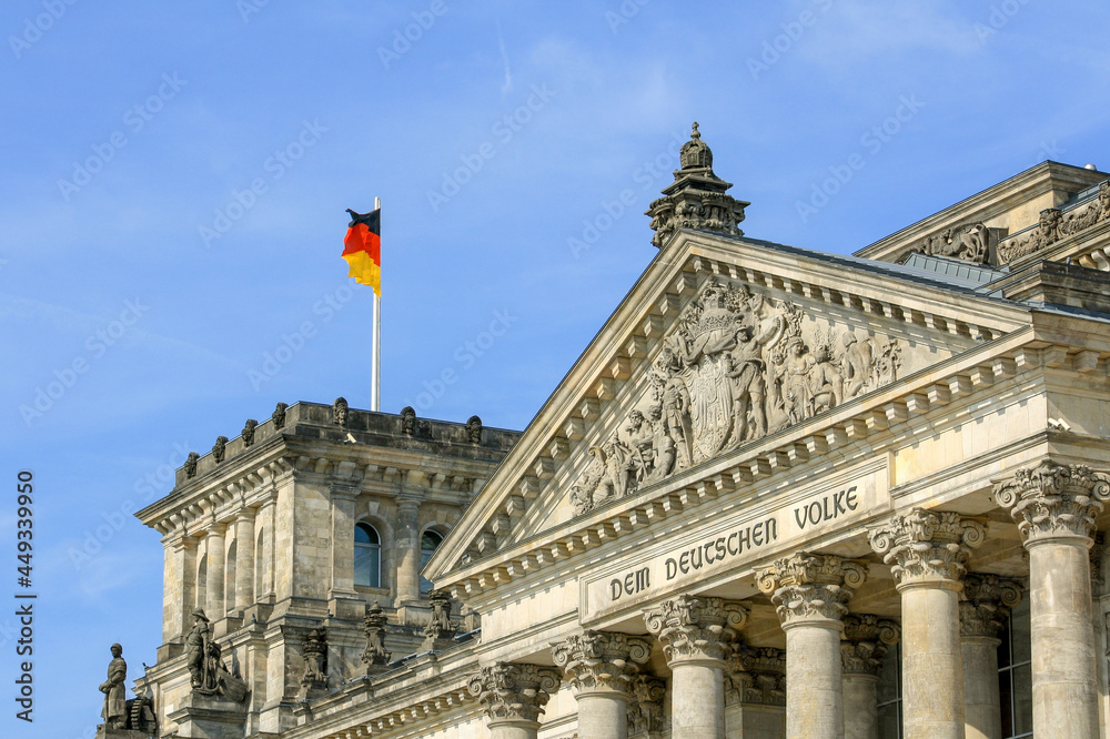 Exterior of Reichstag building with Germany flag on top in summer blue sky with inscription Dem Deutschen Volke (To the German People). No people.