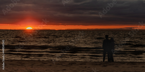 Couple in silhouette standing on a beach at sunset, near Lake Michigan, Ottawa Beach, in Holland State Park, Michigan.