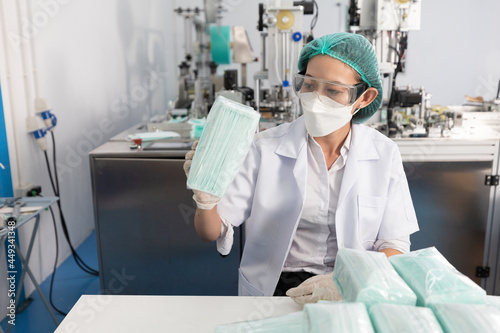 woman factory worker holding packaging a lot of medical face masks and checking of quality from machine