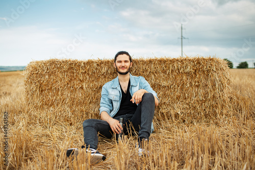 Outdoor portrait of young smiling man, sitting in the wheat field. © Lalandrew