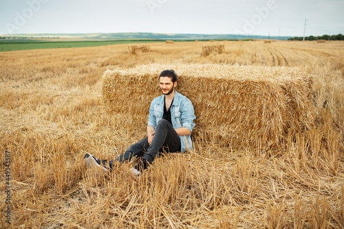 Outdoor photo of young guy in denim jacket, sitting in the wheat field. © Lalandrew