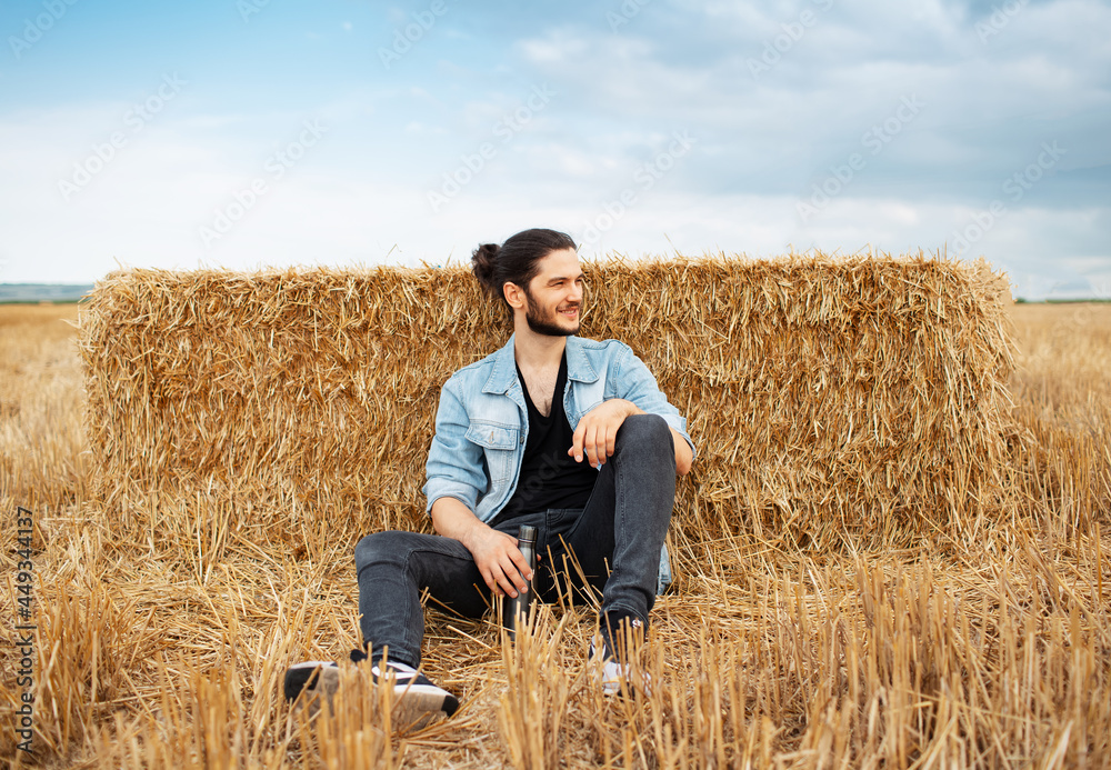 Young guy sitting on background of haystacks in wheat field. Young guy sitting on background of haystacks in wheat field.