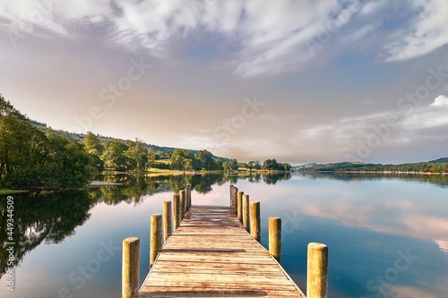 Soft pink early morning light bathes a wooden jetty on Coniston Water in the Lake District, shot in landscape