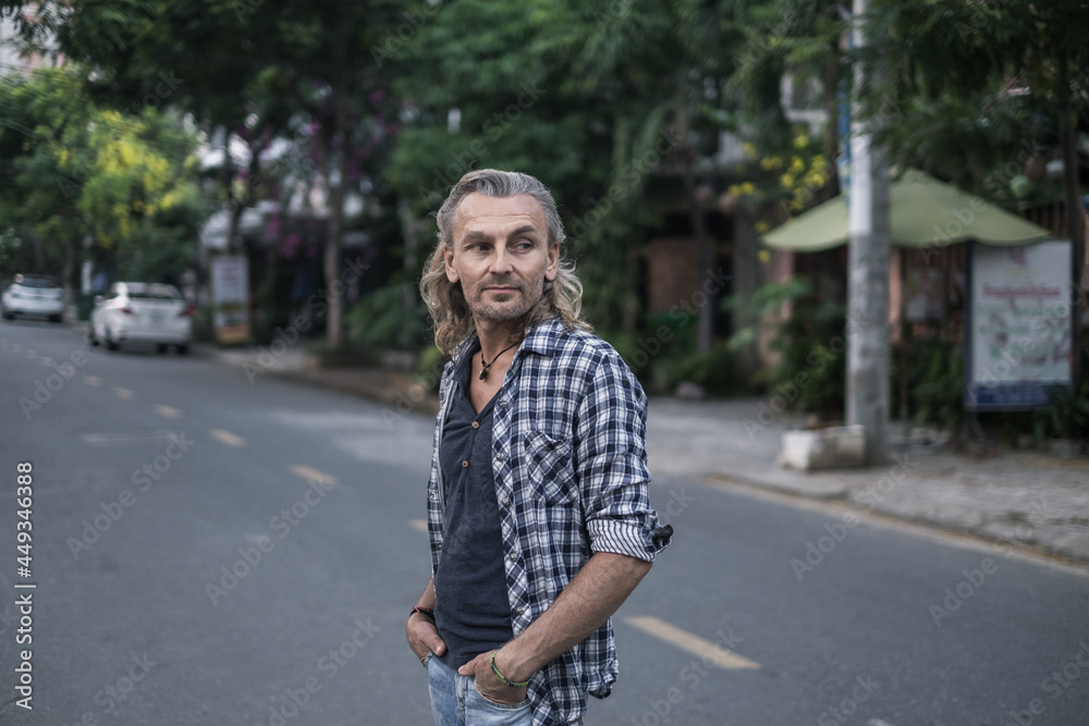 Portrait of mature handsome man in shirt and jeans walking on the street in asia. Long grey hair. Portrait.
