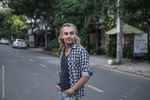 Portrait of mature handsome man in shirt and jeans walking on the street in asia. Long grey hair. Portrait. © Aleksandr