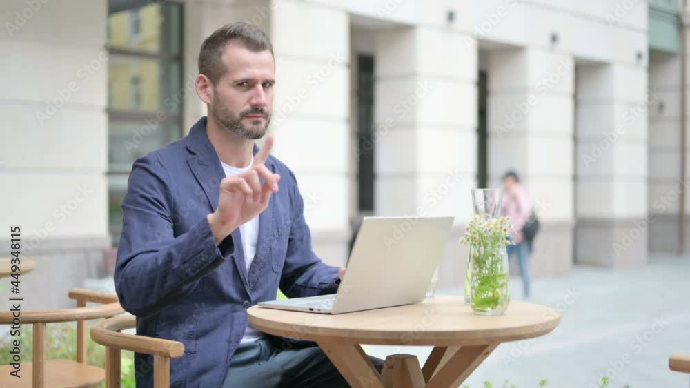 Man showing No Sign while using Laptop, Sitting in Outdoor Cafe Man showing No Sign while using Laptop, Sitting in Outdoor Cafe
