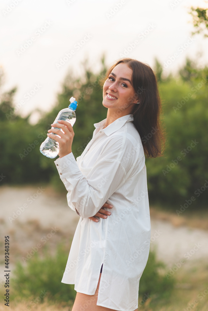 Girl drinks water from a plastic bottle.young caucasian woman in nature forest in woods while holding bottle of water Girl drinks water from a plastic bottle.young caucasian woman in nature forest in woods while holding bottle of water