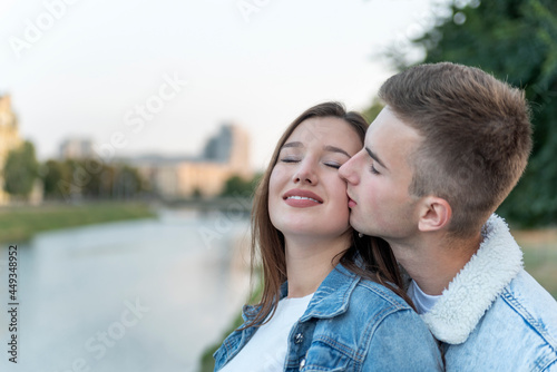 Portrait of young loving couple on river. Guy kisses his beloved on the cheek. Romantic date