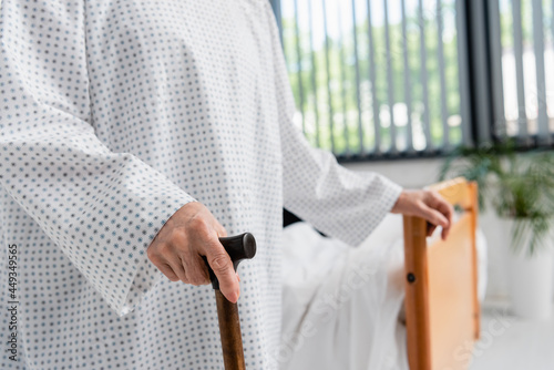 Cropped view of elderly woman in medical gown holding walking cane
