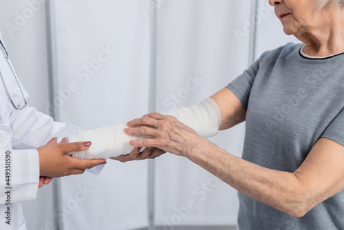 Cropped view of senior woman with plaster bandage on arm standing near african american doctor