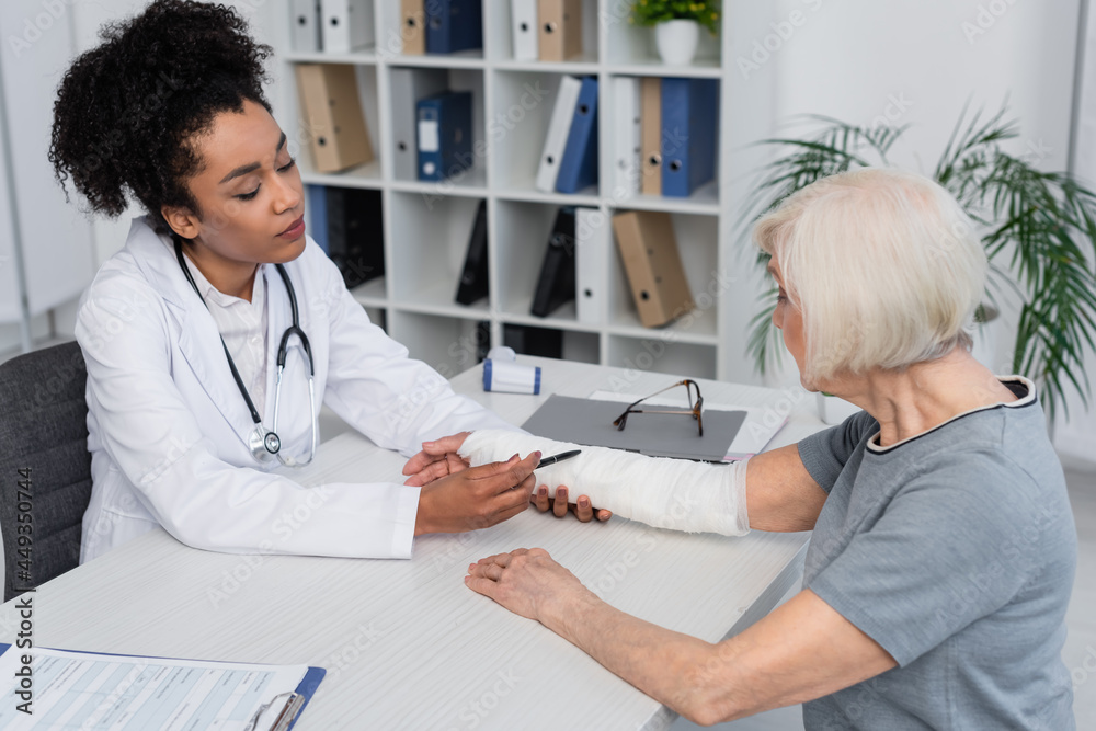 African american doctor pointing at plaster bandage on arm of patient African american doctor pointing at plaster bandage on arm of patient