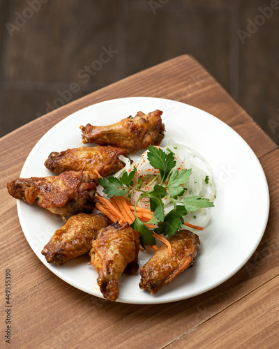 Fried chicken wings, onions, carrot and parsley on white platter. Roasted poultry meat. Food plate on wooden background. Vertical format. Soft focus.