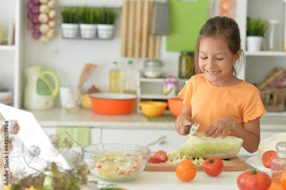 Cute girl making salad on kitchen and using laptop