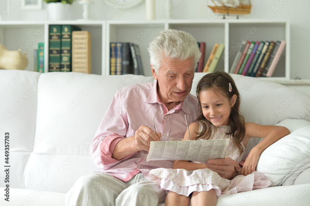 Emotional senior man with girl reading newspaper at home