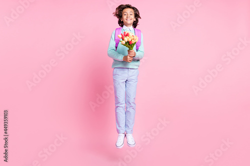 Photo of funny schoolboy jump hold tulips bunch celebrate wear bag teal shirt pants shoes isolated pink color background