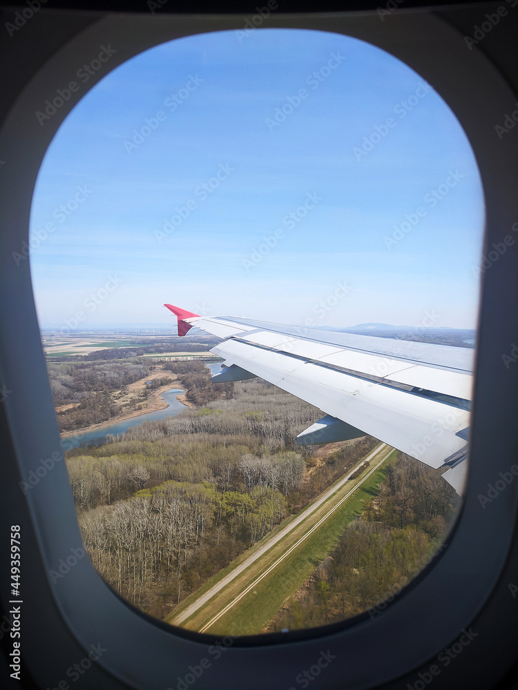 Beautiful window view of blue sky and fluffy clouds from passenger seat on airplane. View of many windmills at big green meadows. Concept of travel and air transportation.
