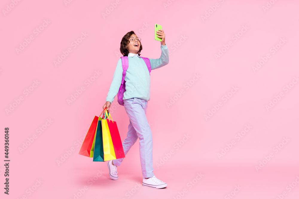 Photo of excited schoolboy walk hold bags telephone wear bag glasses teal shirt isolated pink color background Photo of excited schoolboy walk hold bags telephone wear bag glasses teal shirt isolated pink color background