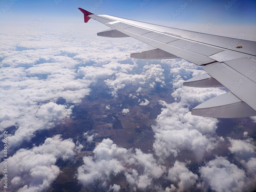 Obraz premium Beautiful window view of blue sky and fluffy clouds from passenger seat on airplane. View of many windmills at big green meadows. Concept of travel and air transportation.