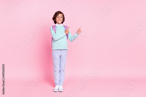 Photo of little schoolkid direct finger empty space wear bag spectacles teal shirt isolated pink color background