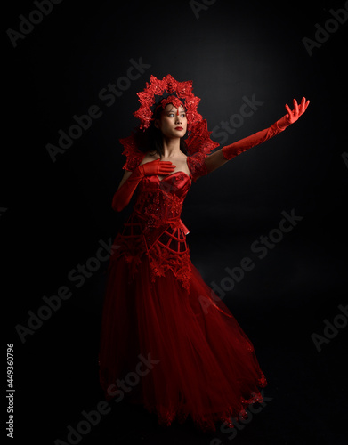 Full length  portrait of beautiful young asian woman wearing red corset, long opera gloves and ornate gothic queen crown. Graceful posing isolated on a dark studio background.