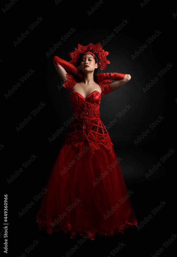 Full length portrait of beautiful young asian woman wearing red corset, long opera gloves and ornate gothic queen crown. Graceful posing isolated on a dark studio background. Full length portrait of beautiful young asian woman wearing red corset, long opera gloves and ornate gothic queen crown. Graceful posing isolated on a dark studio background.
